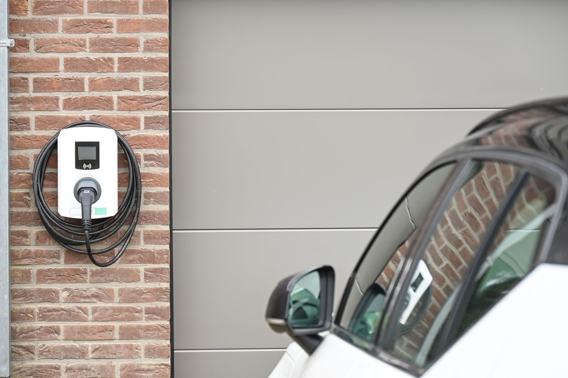 Recharge de voiture électrique à une borne murale fixée à côté d'un mur de briques et d'une porte de garage.