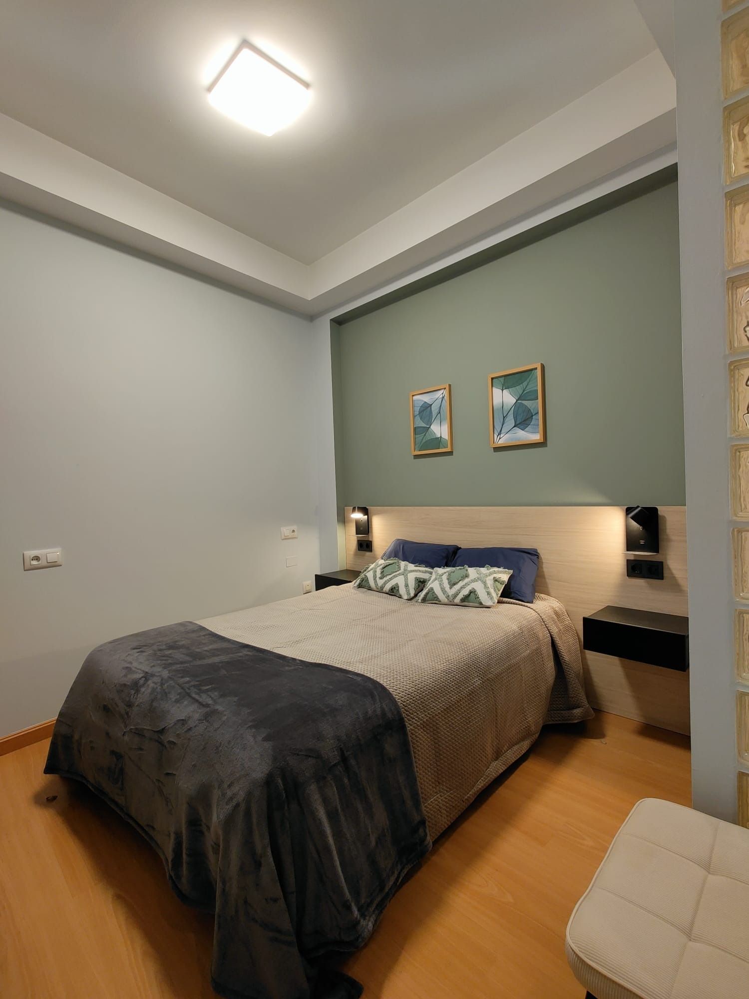 Dormitorio con cama, mesitas de noche y obras de arte. La pared detrás de la cama es verde, con paredes grises en el resto.