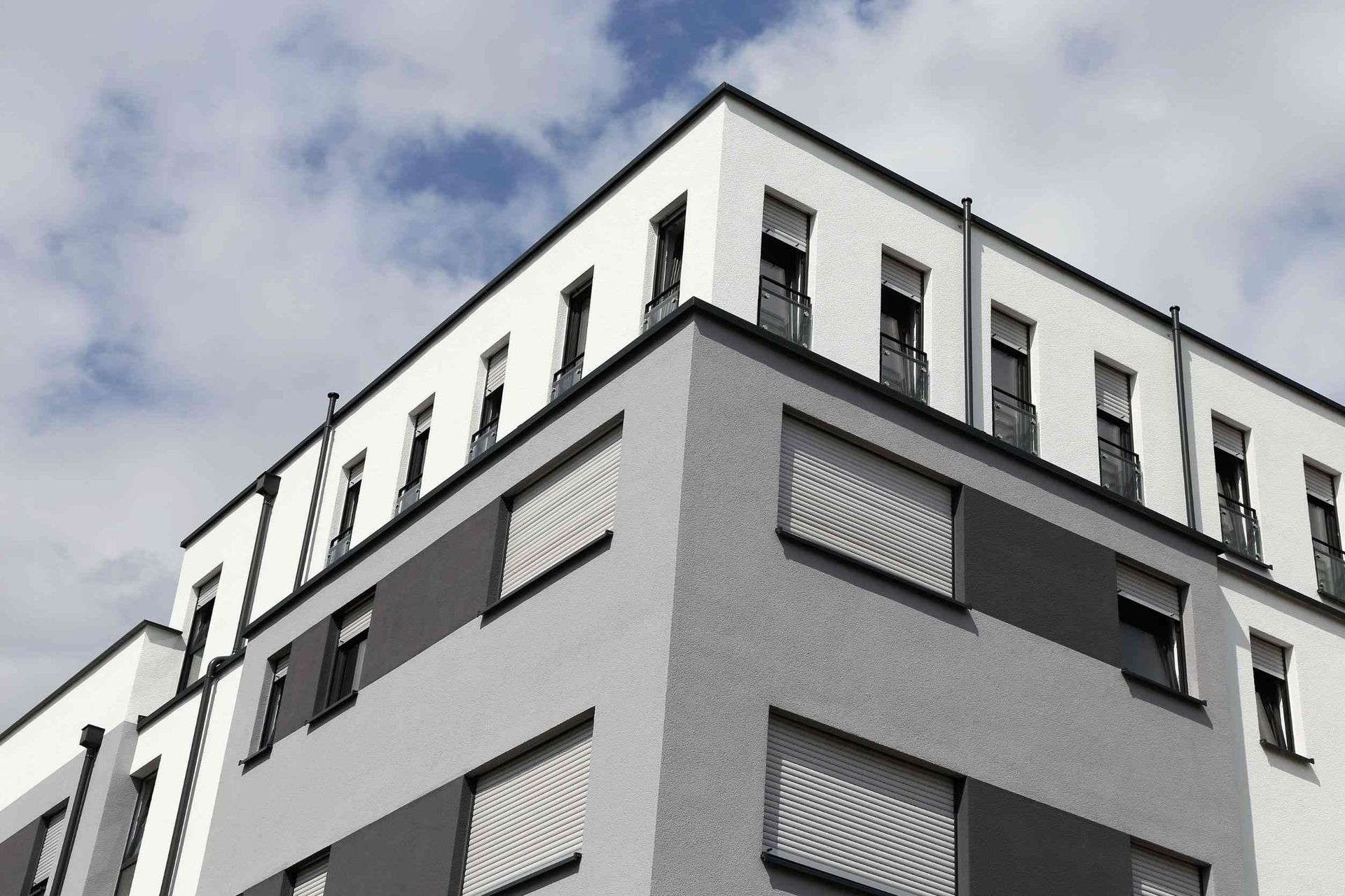 Edificio moderno de varios pisos con fachada blanca y gris contra un cielo parcialmente nublado.