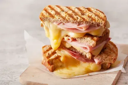 Un sándwich de jamón y queso a la parrilla se apila uno encima del otro sobre una tabla de cortar de madera.