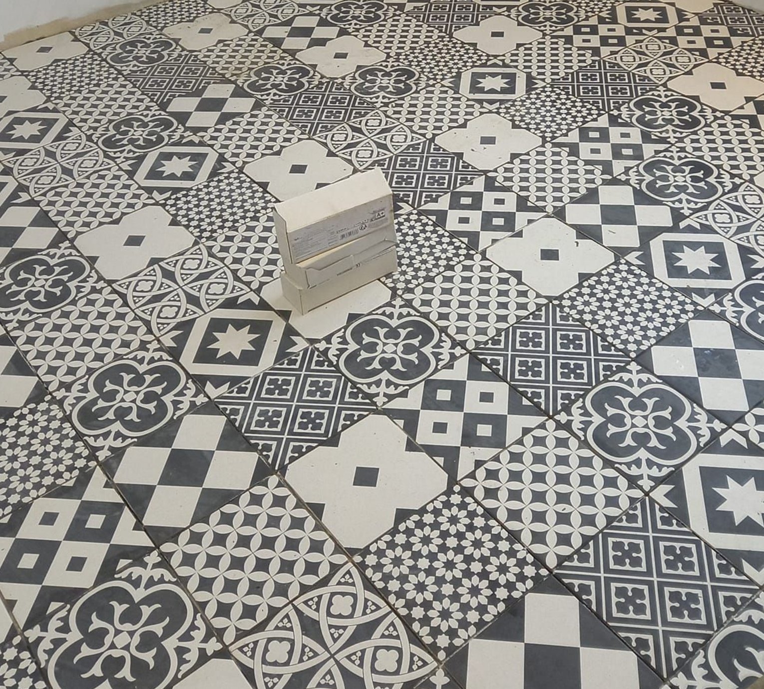 Sol carrelé à motifs noirs et blancs avec un empilement de carreaux rectangulaires au centre.