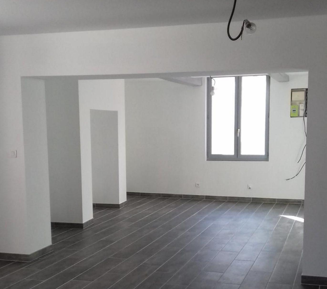 Pièce en cours de démolition, un ouvrier se tient à proximité. Des débris jonchent le sol. Des étais soutiennent les murs.