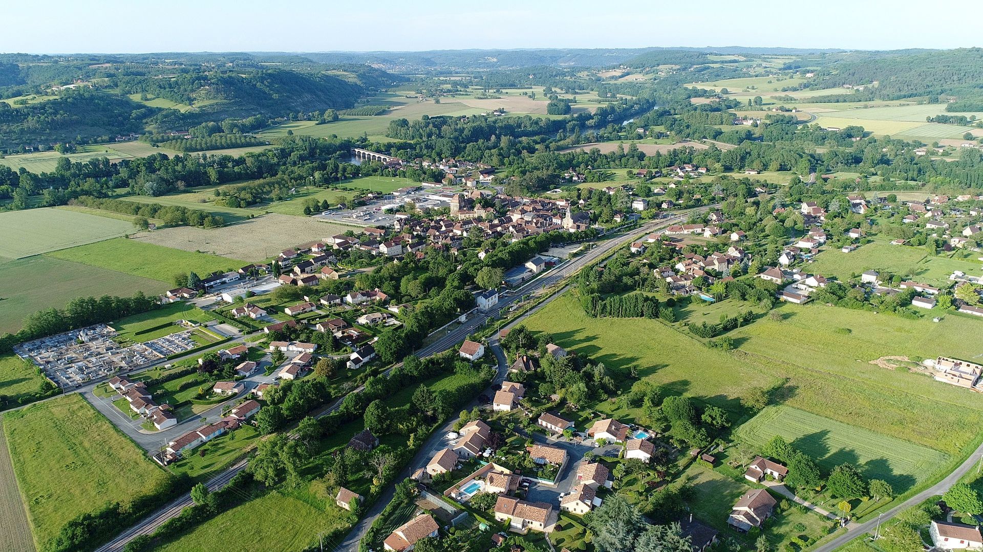 Vue aérienne d'une ville nichée dans une vallée, entourée de champs verdoyants et de collines ondulantes.