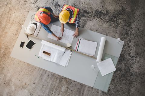 Deux ouvriers du bâtiment, casques de chantier sur la tête, examinent des plans à une table sur un chantier.