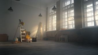 Pièce vide avec outils de rénovation, grandes fenêtres laissant entrer la lumière du soleil.