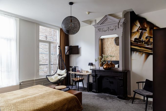 Lichte slaapkamer met bed, hangstoel, sierlijke open haard en groot raam met transparante gordijnen.