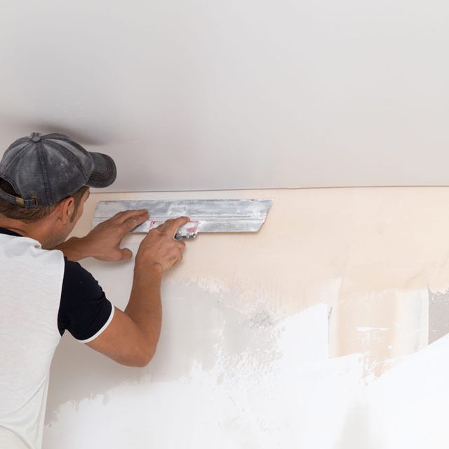 Un hombre está usando una espátula para quitar el papel tapiz de una pared.