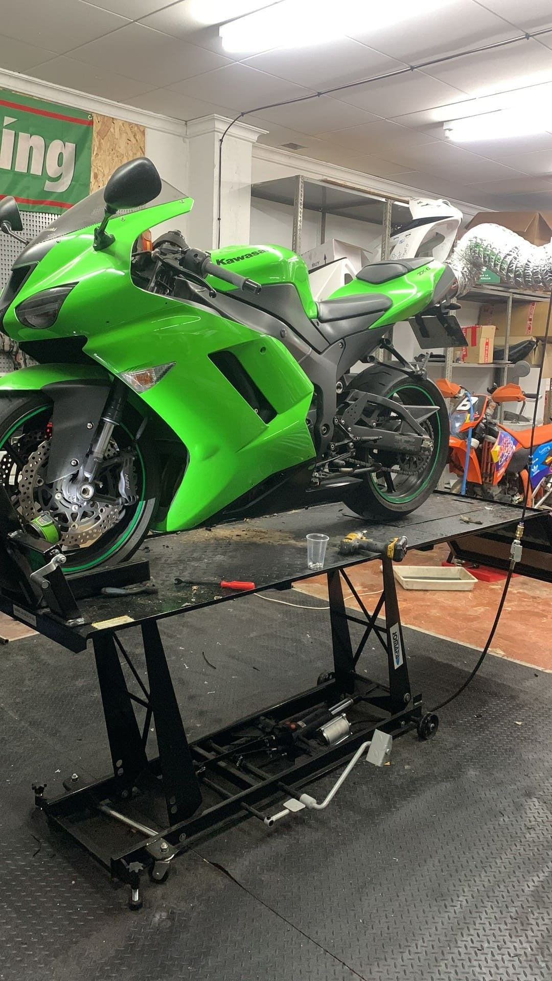Una motocicleta verde está parada encima de un elevador en un garaje.