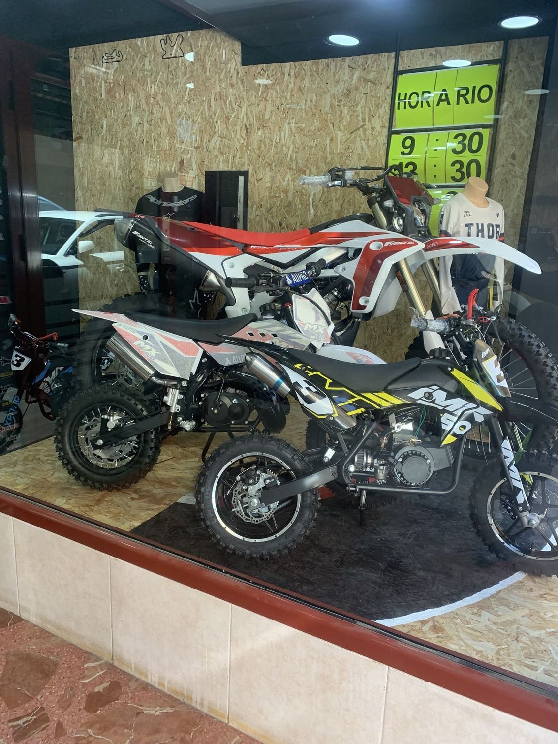 Una fila de motos de cross están estacionadas en el escaparate de una tienda.