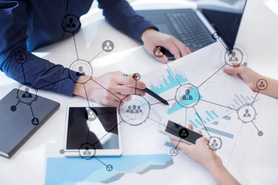 Reunión de negocios con intercambio de documentos, tableta y computadora portátil, conectados por iconos de red en un escritorio.