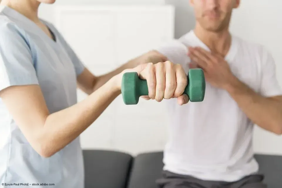 Eine Therapeutin in blauer Arbeitskleidung verwendet in einer medizinischen Einrichtung einen stacheligen Massageball an der Hand eines Patienten.