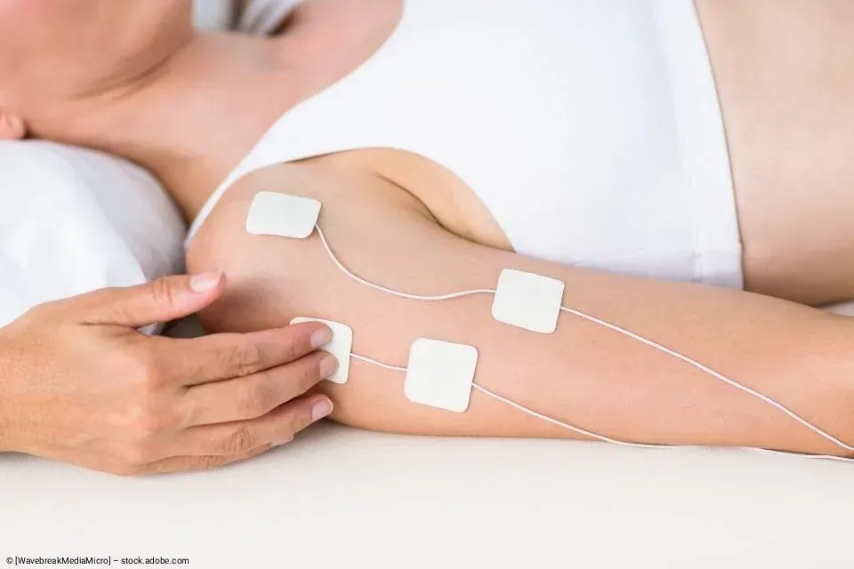 Hand, die während einer medizinischen Behandlung weiße Klebeelektrodenpads mit angeschlossenen Drähten auf einem nackten Bein verwendet