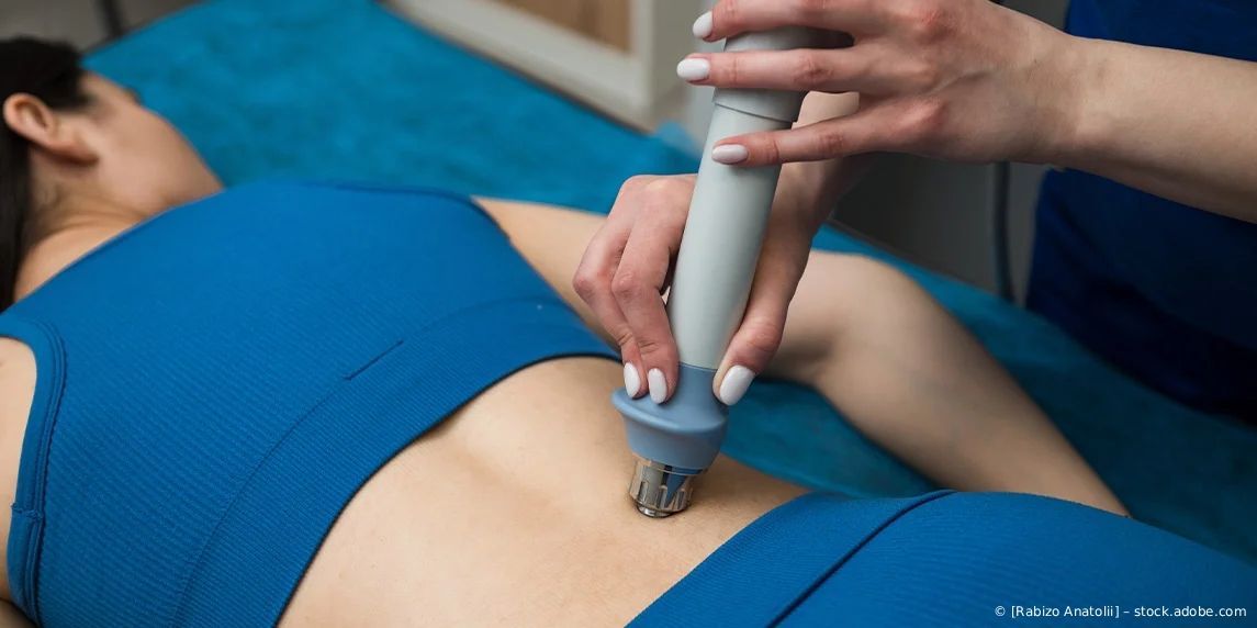 Therapeut verwendet während einer Behandlungssitzung ein Handgerät am unteren Rücken des Patienten.