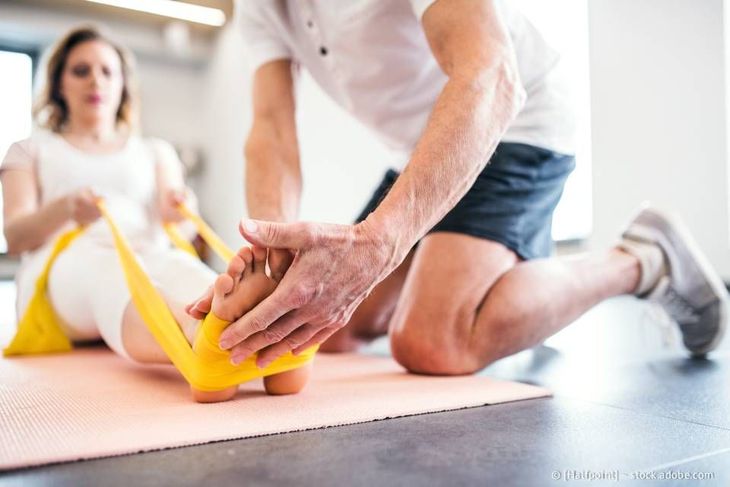 Eine Person hilft einer anderen Person bei Physiotherapieübungen mit Hilfe eines Widerstandsbandes.