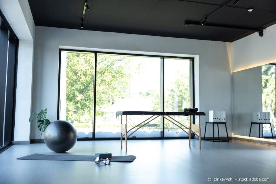 Yogastudio mit Gymnastikball, Matte und Ausrüstung in der Nähe großer Fenster mit Blick ins Freie.