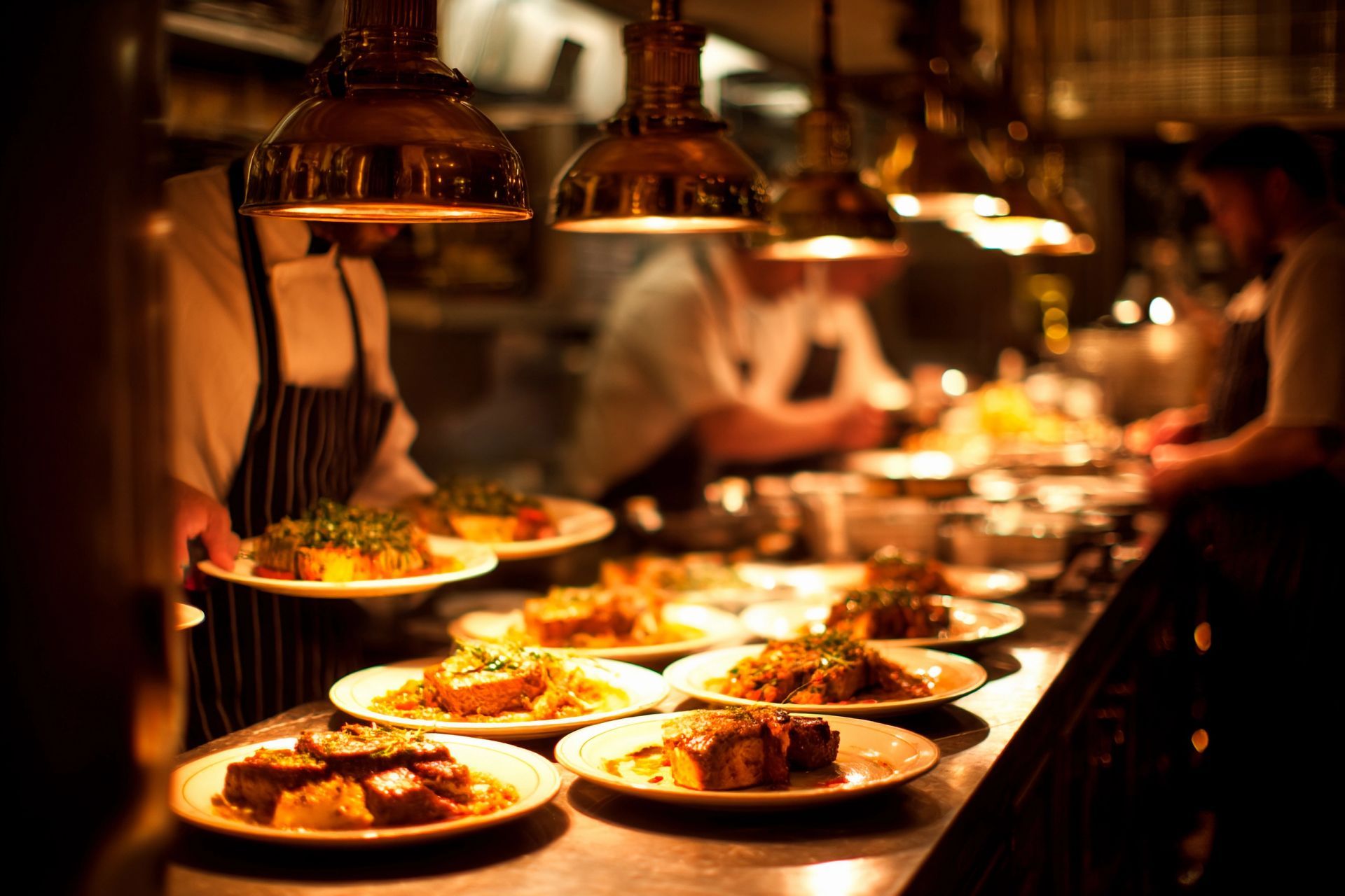 Köche richten Speisen an einem warm beleuchteten Restaurantbuffet unter Kupferwärmelampen an.