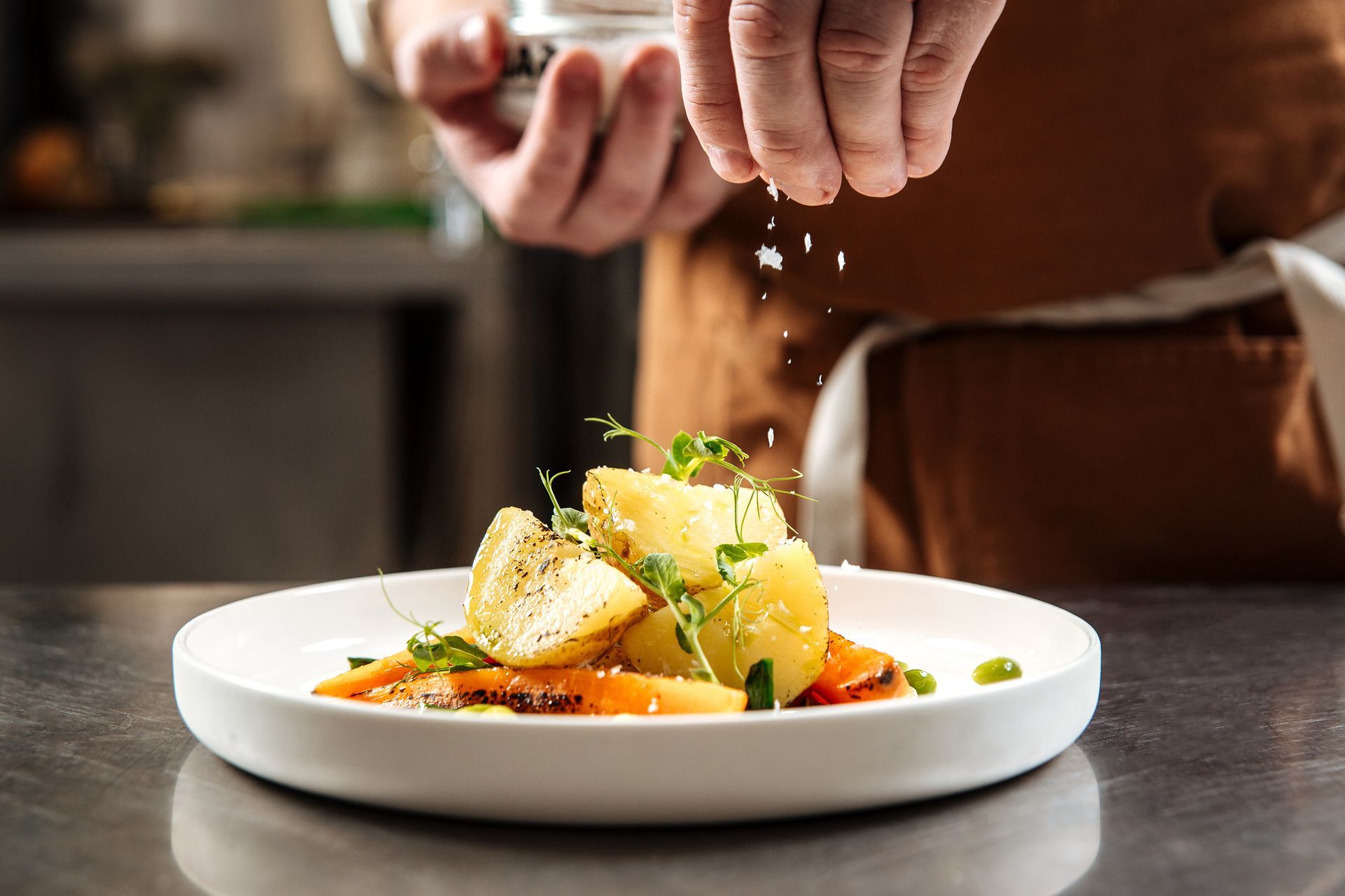 Ein Koch garniert ein angerichtetes Gericht mit Kräutern in der Restaurantküche.
