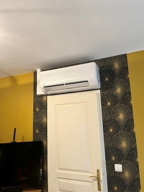 Module de pompe à chaleur au-dessus d'une porte, pièce avec mur tapissé et peinture couleur moutarde