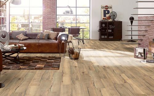 Salon avec parquet, canapé en cuir, murs en briques apparentes et grandes fenêtres.