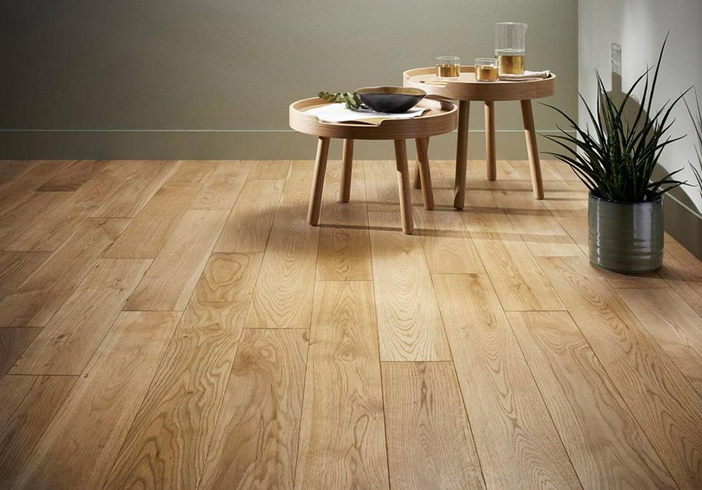 Sol en bois, deux petites tables et une plante en pot dans une pièce aux murs verts.