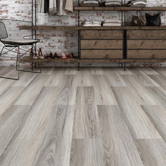 Sol en planches de bois dans une pièce avec un placard de style rustique et un mur de briques en arrière-plan ; une chaise est placée à gauche.