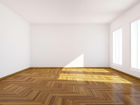 Pièce vide avec parquet en bois et deux fenêtres, éclairée par la lumière du soleil.