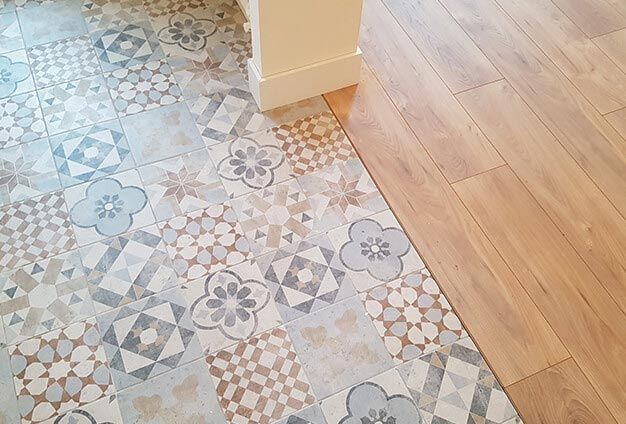 Un sol carrelé à motifs côtoie un parquet en bois, à côté d'une colonne blanche.