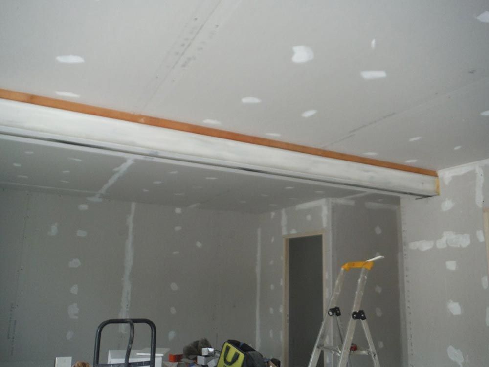 Pièce intérieure avec cloisons sèches non finies, poutre en bois et échelle.