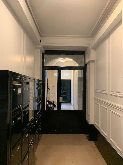 Couloir avec boîtes aux lettres à gauche, une porte noire au fond et des murs lambrissés blancs.