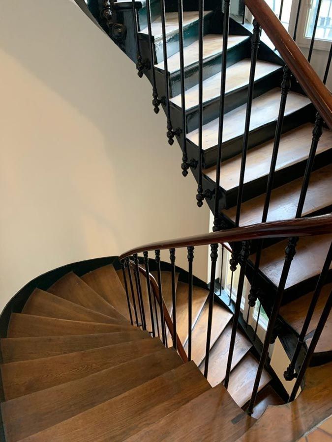 Escalier en colimaçon en bois avec rampes noires et main courante en bois foncé, dans une pièce aux murs blancs.