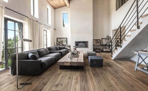 Salon spacieux avec canapé gris, parquet, cheminée et escalier.