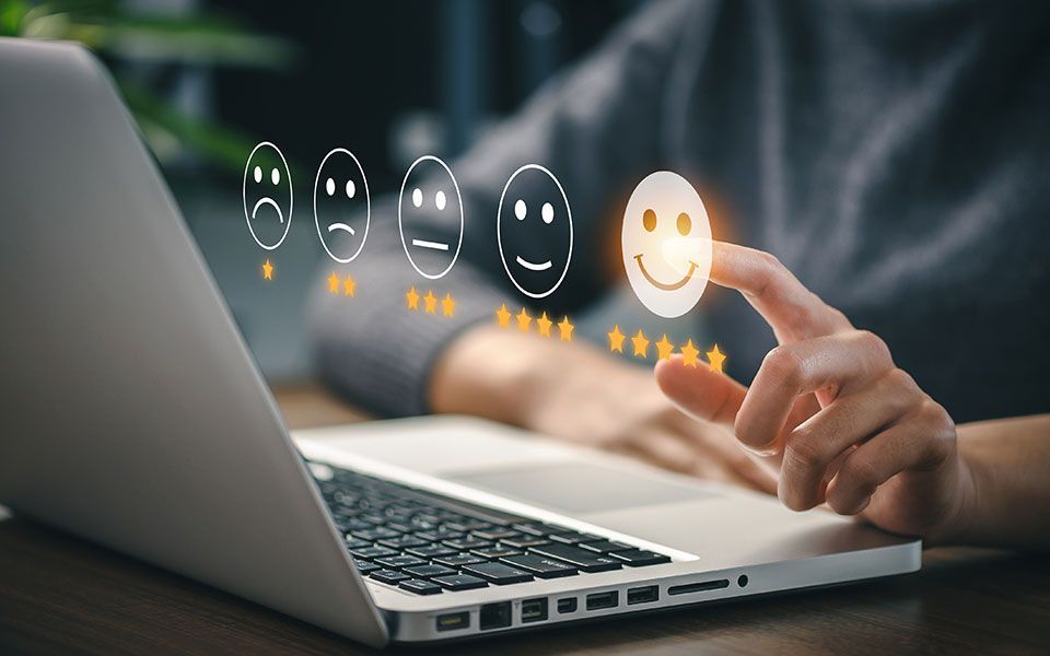 Une personne donne un avis positif sur un ordinateur portable, en sélectionnant une icône de visage souriant avec son doigt.
