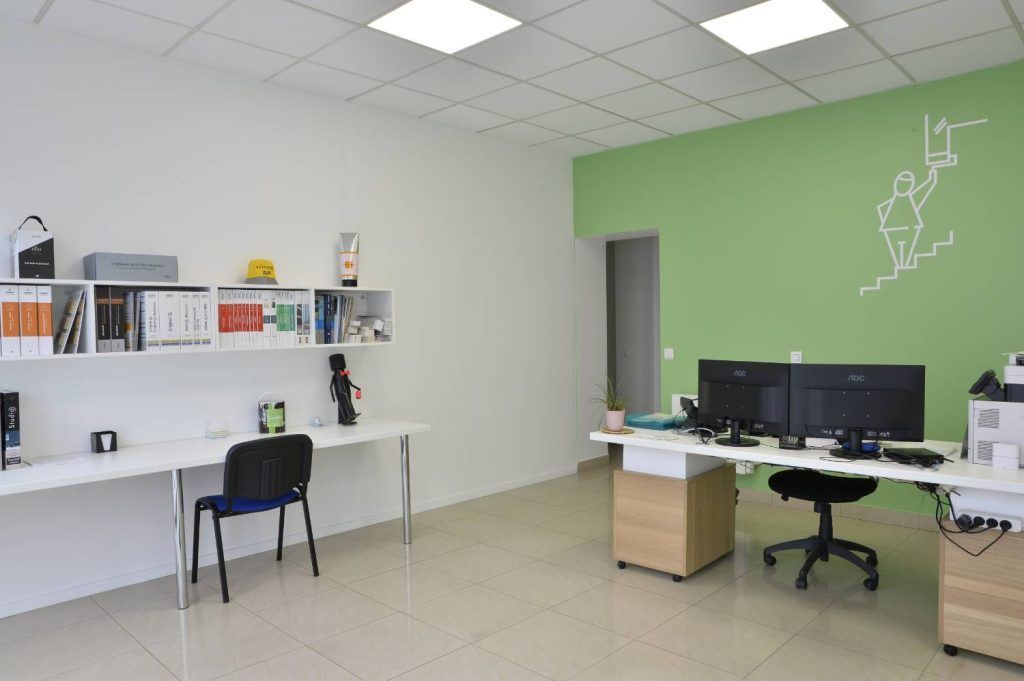 Espace de bureau avec bureaux, ordinateurs, étagères de rangement et un mur d'accent vert orné d'un croquis représentant une silhouette montant un escalier.