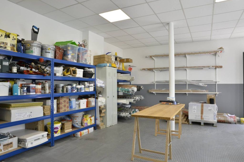 Intérieur d'atelier avec étagères bleues, outils, établi et colonne de soutien.