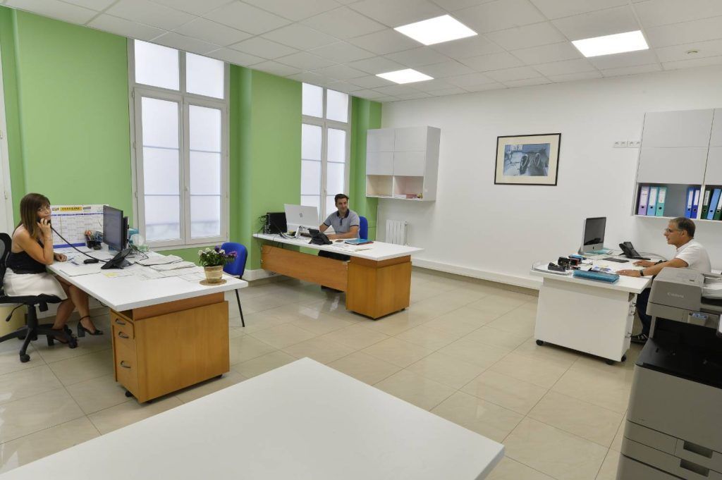 Intérieur de bureau avec trois personnes travaillant à des bureaux, un mur d'accent vert et un éclairage vif.