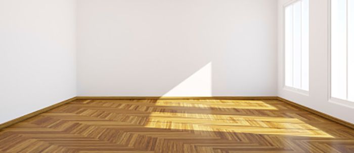 Pièce vide avec parquet et murs blancs. La lumière du soleil entre par une fenêtre.