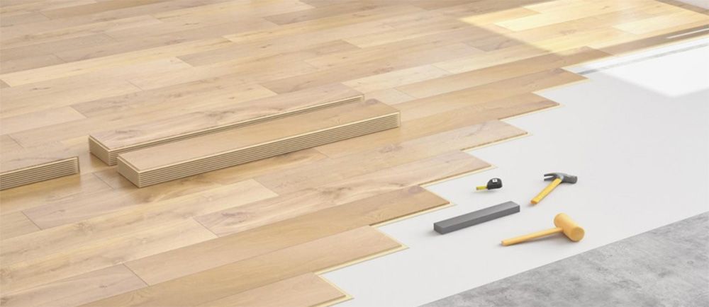 Pose d'un parquet en bois dur avec lames emboîtables, outils et sous-couche sur béton.