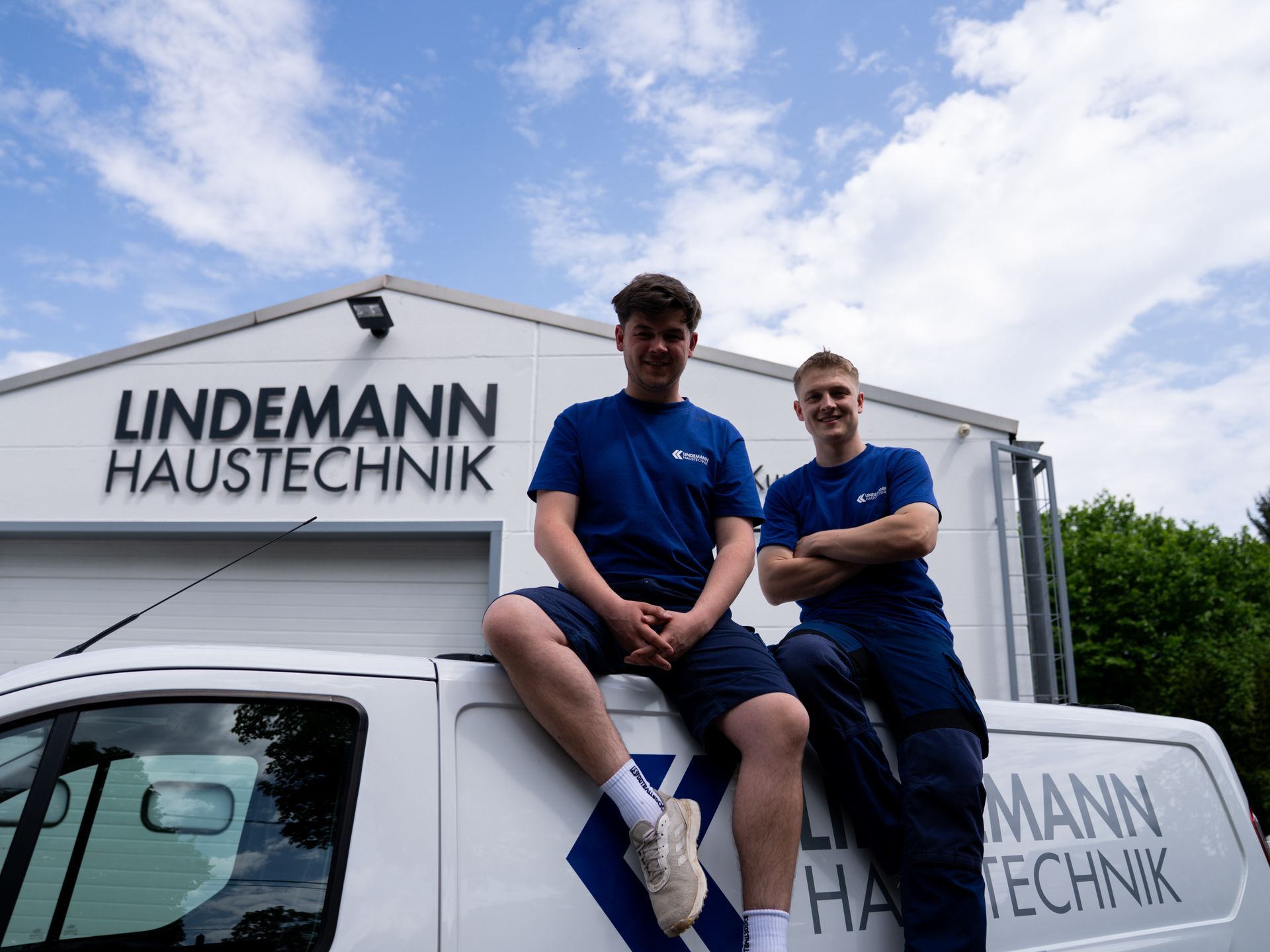 Zwei Männer sitzen auf einem Lieferwagen vor einem Gebäude.