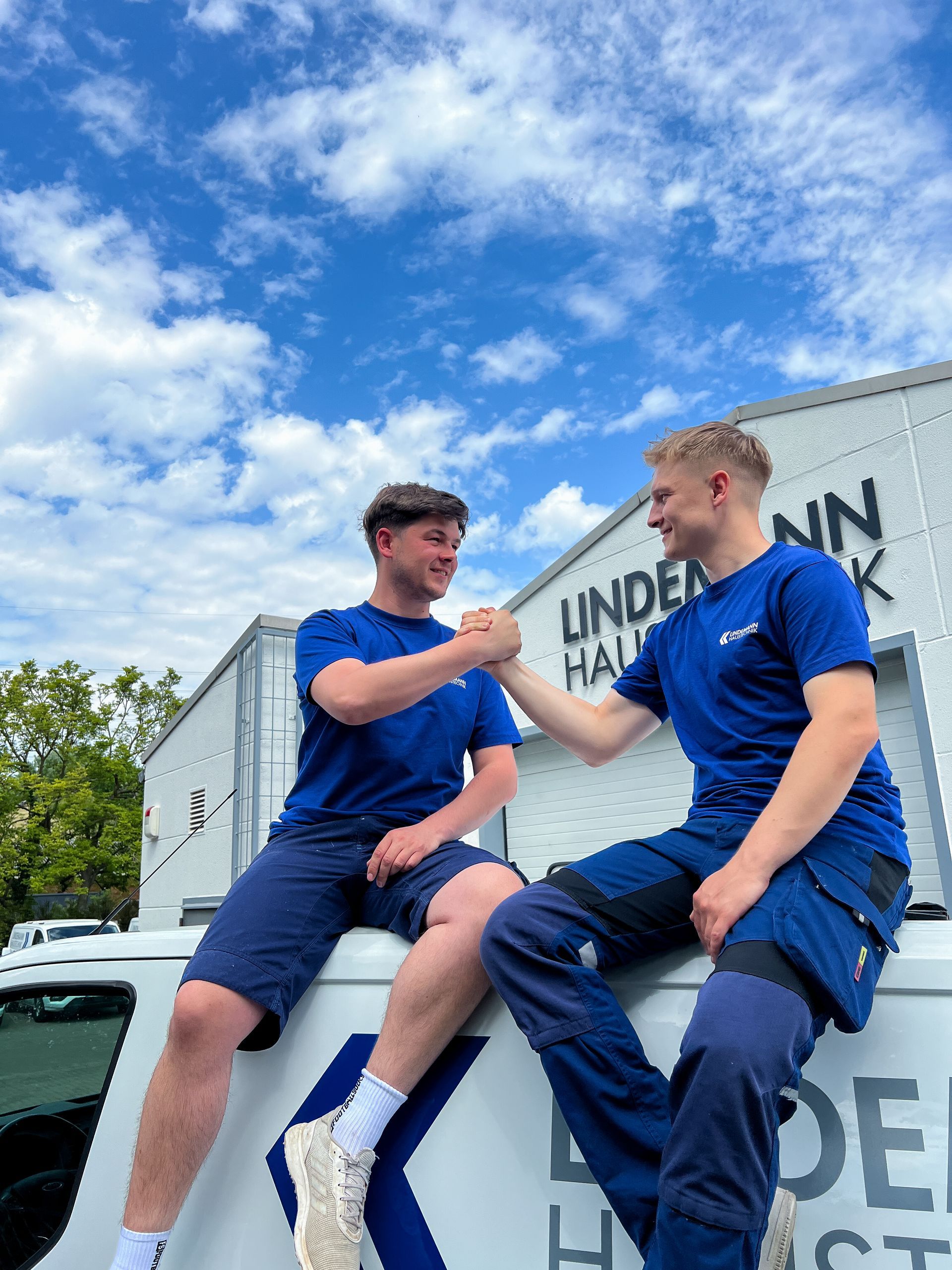 Zwei Männer sitzen auf der Seite eines Lastwagens und schütteln sich die Hände.