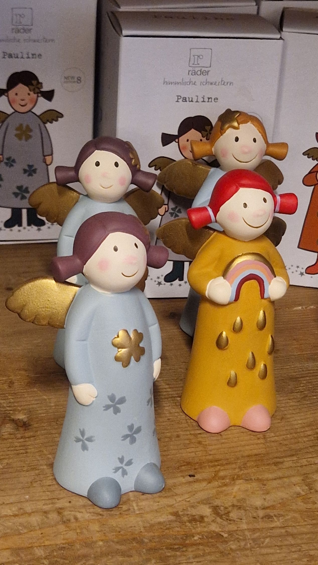 Kleine Engelfiguren aus Keramik mit goldenen Flügeln in Blau, Gelb und Braun und lächelnden Gesichtern.