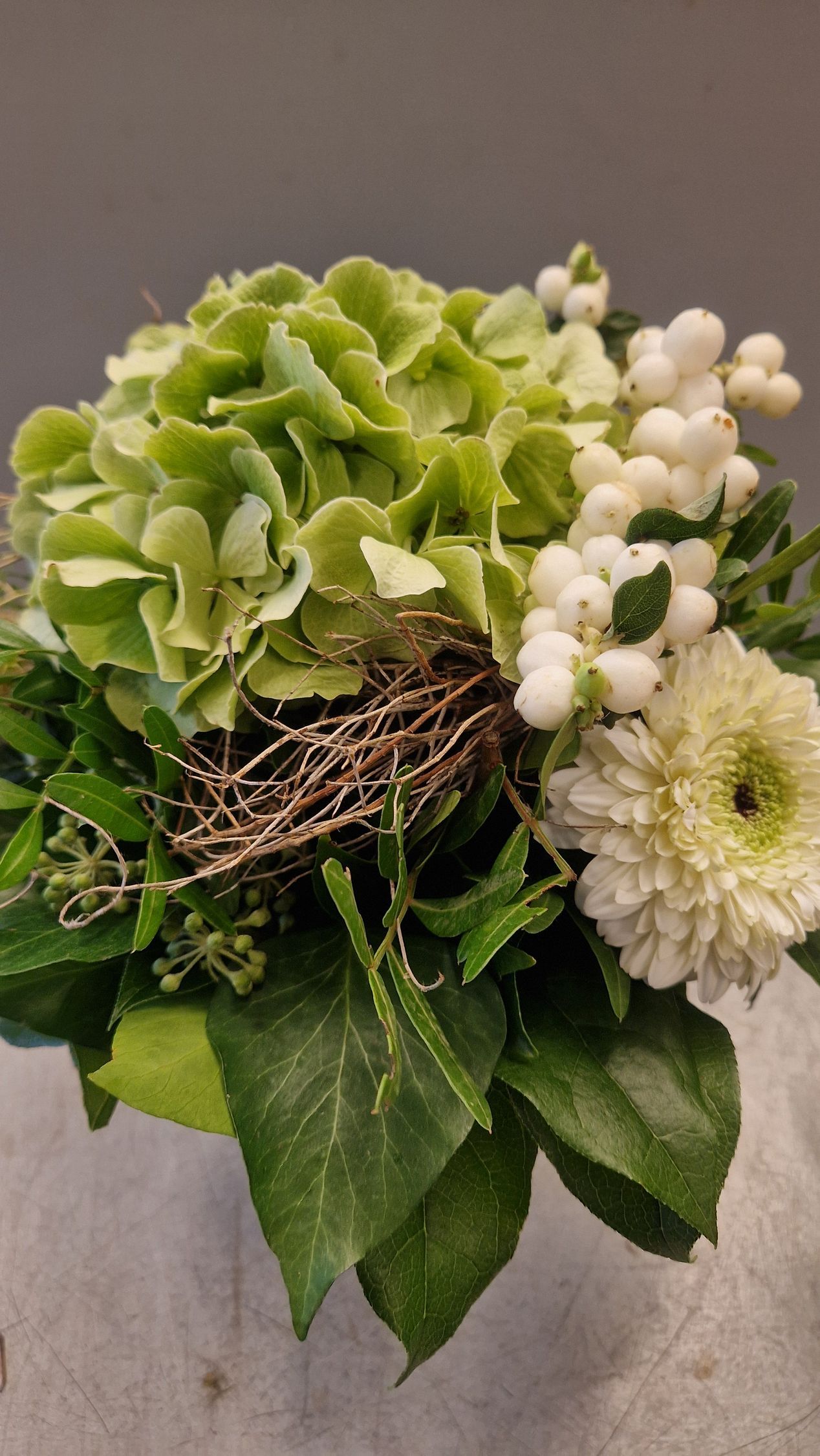 Grüne Hortensien und weiße Blüten in einem Blumenarrangement mit Grünpflanzen.