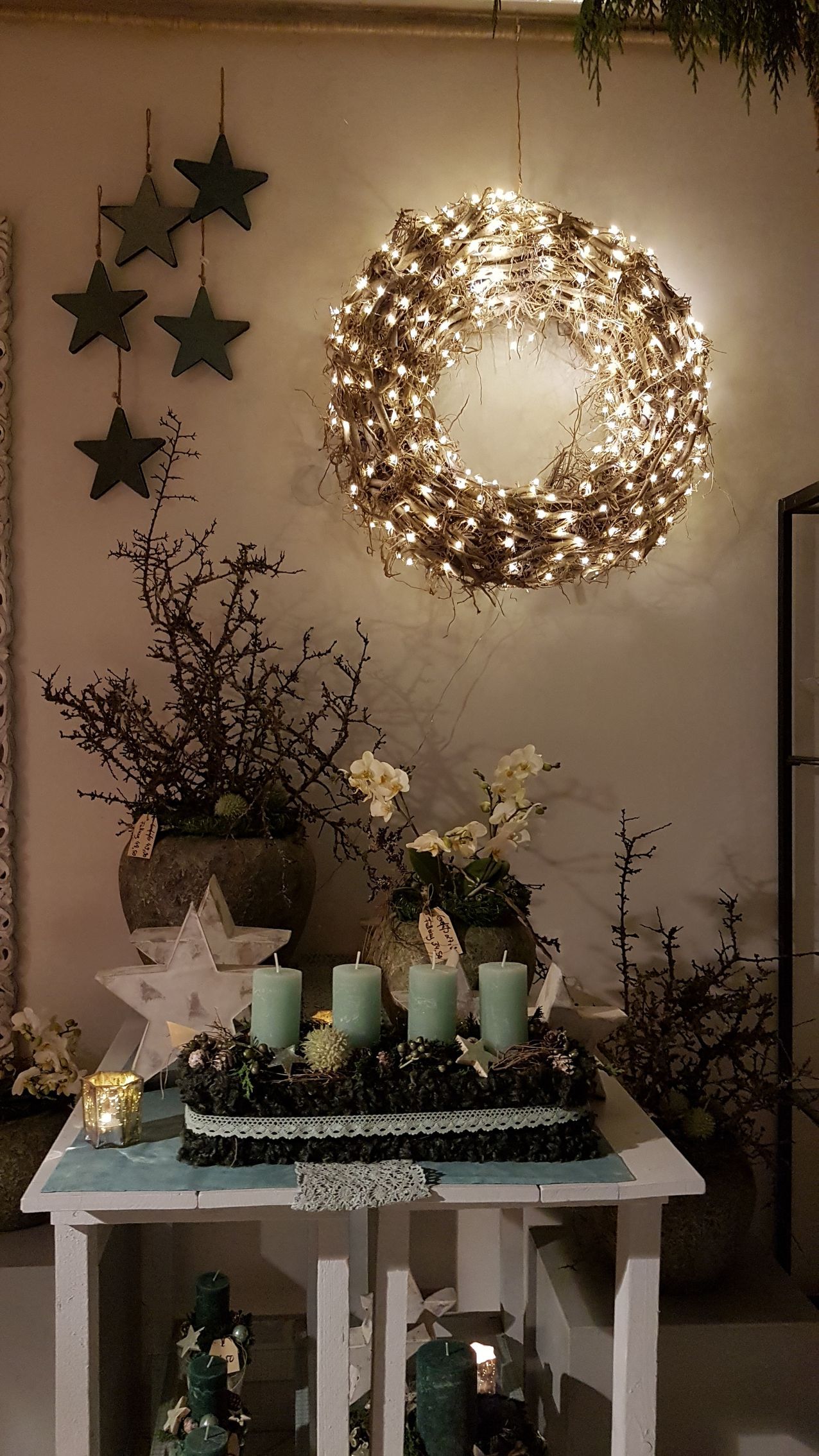 Weihnachtsdekoration: beleuchteter Kranz, Adventskerzen, Sternornamente und Dekorationen auf einem weißen Tisch.