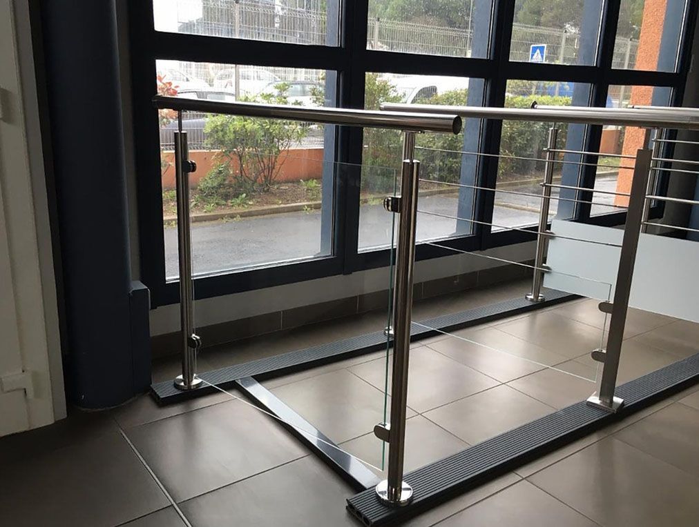 Garde-corps en acier inoxydable avec panneaux de verre jouxtant de grandes fenêtres donnant sur un bâtiment extérieur.