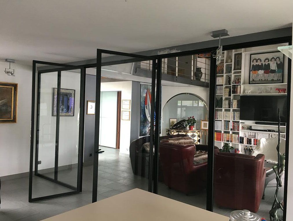 Cloisons vitrées dans un espace de vie agrémenté d'œuvres d'art, de chaises rouges et d'une bibliothèque blanche.