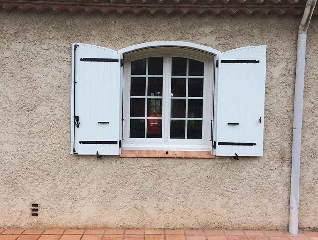 Fenêtre à cadre blanc avec volets ouverts sur un mur beige texturé, sol en carrelage de terre cuite.