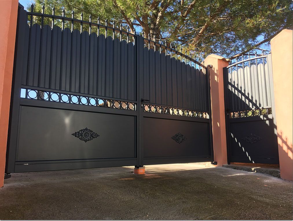Portail d'allée en métal noir avec détails décoratifs et barreaux verticaux.