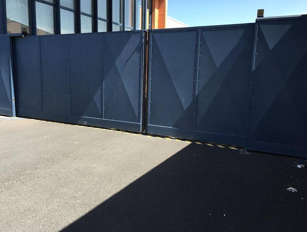 Portail métallique bleu foncé à motif losanges, fermé sur asphalte.