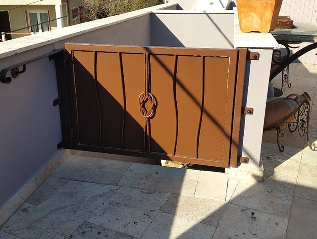 Portail en métal marron sur une terrasse, fixé à un mur gris.