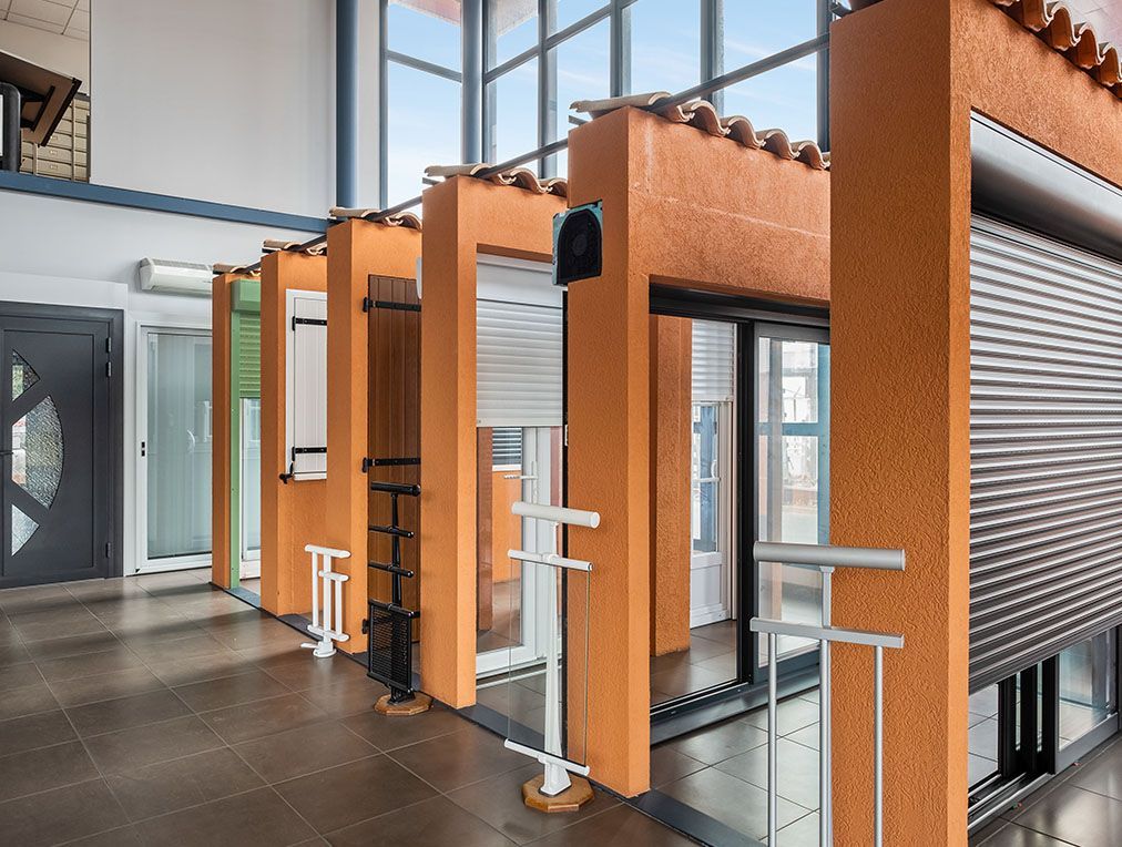 Présentation de différents styles de fenêtres et de portes, notamment de volets roulants, dans un espace d'exposition.