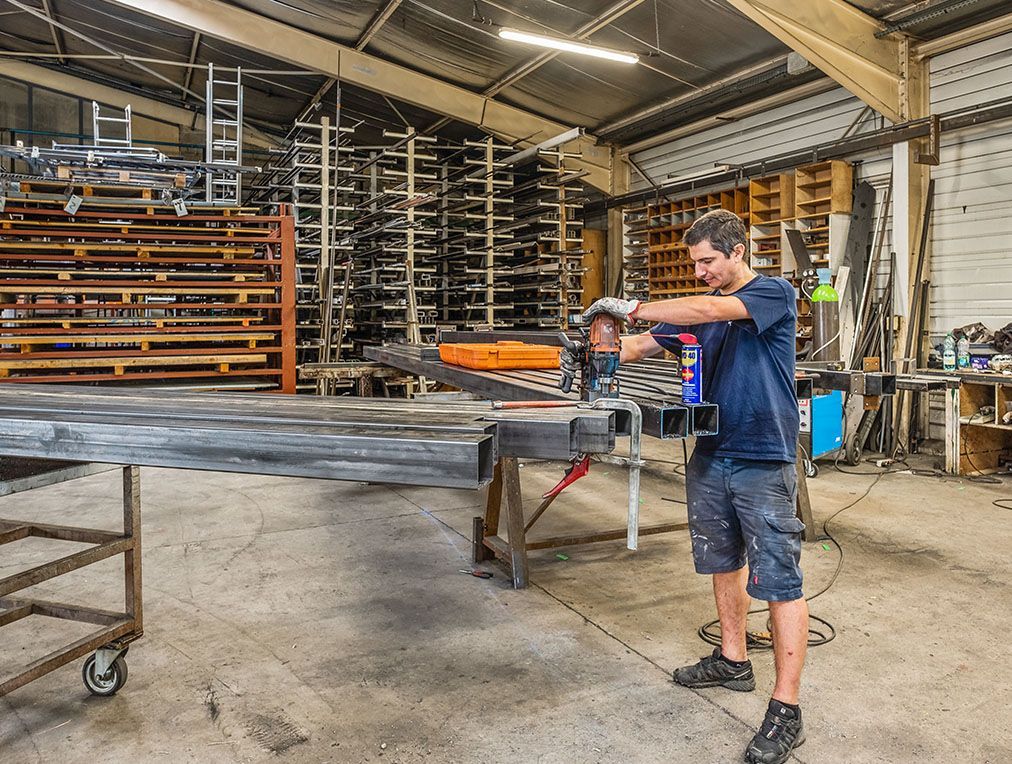 Un homme utilise un outil pour couper du métal dans un atelier, entouré de matériaux et d'étagères.